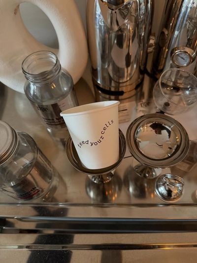A paper cup with 'feed your cells' printed on it, sitting between RIPE bottles and prep glassware